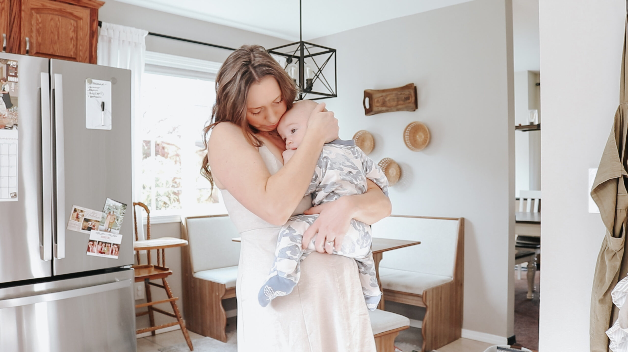 Christian homemaker cuddles her baby close in the kitchen of her home. The baby is in pajamas and the homemaker is wearing a dress.